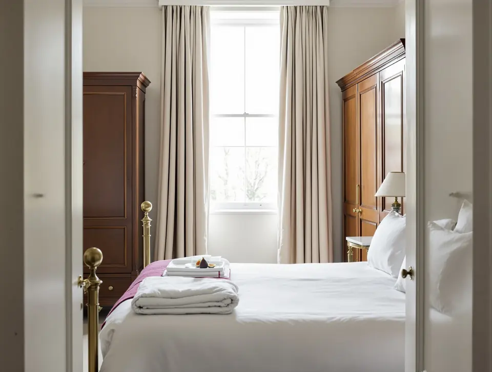 A small Georgian bedroom with antique brass bed and morning light through the sash window.